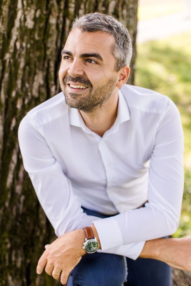 Joachim Metzler Gründer von Erschaffe ist mit weißem Hemd in der Natur neben einem Baum zu sehen.